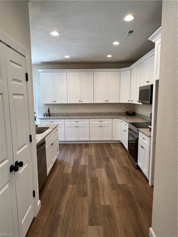 kitchen with appliances with stainless steel finishes, light stone counters, a textured ceiling, white cabinets, and dark hardwood / wood-style floors