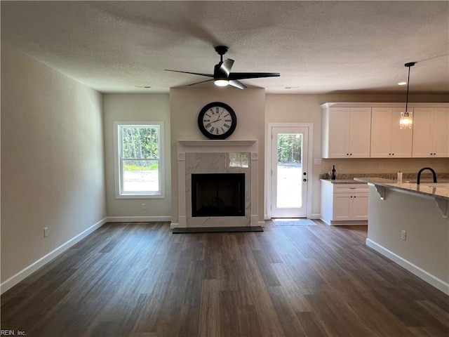 unfurnished living room with a textured ceiling, dark hardwood / wood-style flooring, a healthy amount of sunlight, and a premium fireplace