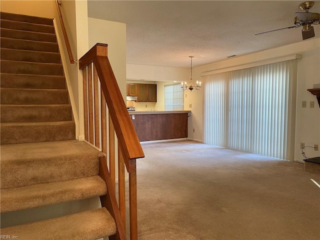 stairway with ceiling fan with notable chandelier, carpet floors, and a textured ceiling