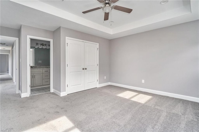 unfurnished bedroom featuring a closet, ceiling fan, light colored carpet, and a tray ceiling