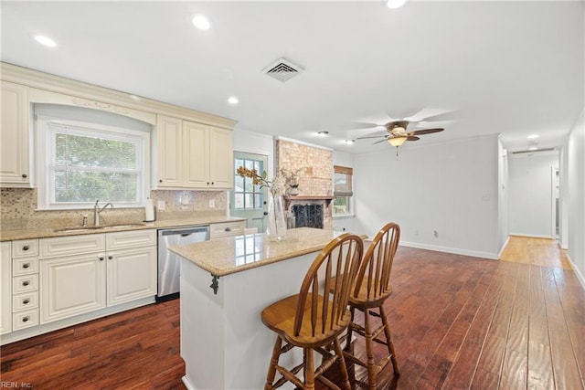 kitchen with sink, dark wood-type flooring, tasteful backsplash, stainless steel dishwasher, and a kitchen island