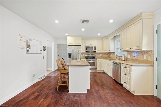 kitchen with cream cabinetry, appliances with stainless steel finishes, a center island, and dark wood-type flooring