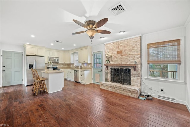 kitchen with appliances with stainless steel finishes, a kitchen breakfast bar, a fireplace, a center island, and dark hardwood / wood-style floors