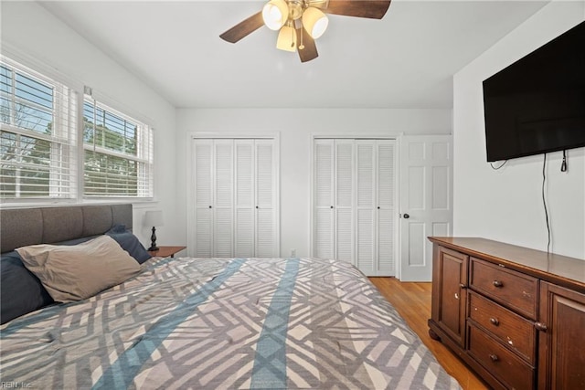 bedroom featuring two closets, light hardwood / wood-style flooring, and ceiling fan