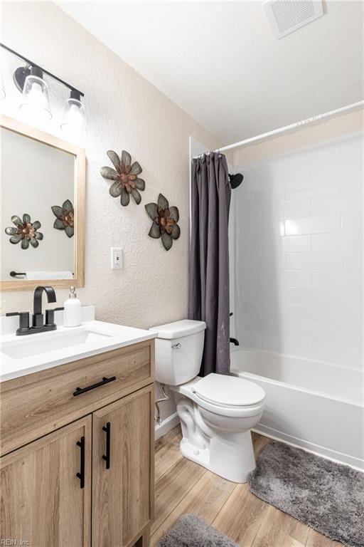 full bathroom with vanity, hardwood / wood-style floors, shower / bathtub combination with curtain, and toilet