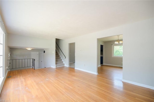 unfurnished living room with an inviting chandelier and light wood-type flooring