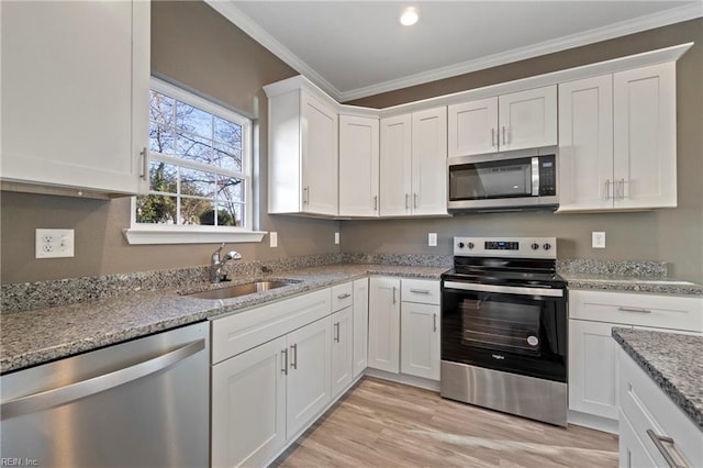 kitchen with white cabinetry, sink, light stone counters, appliances with stainless steel finishes, and ornamental molding