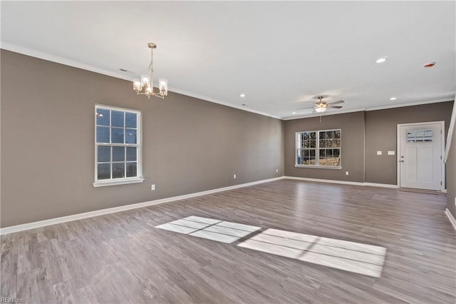 empty room with crown molding, hardwood / wood-style floors, a healthy amount of sunlight, and ceiling fan with notable chandelier