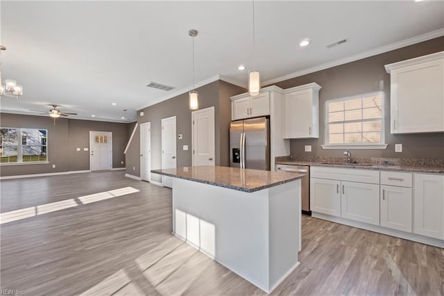 kitchen featuring a healthy amount of sunlight, stainless steel appliances, pendant lighting, white cabinets, and ceiling fan with notable chandelier