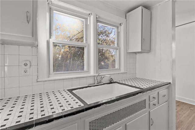 kitchen with light wood-type flooring, backsplash, sink, white cabinetry, and tile counters