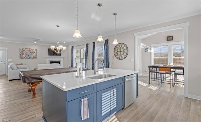 kitchen featuring a center island with sink, sink, stainless steel dishwasher, light wood-type flooring, and decorative light fixtures