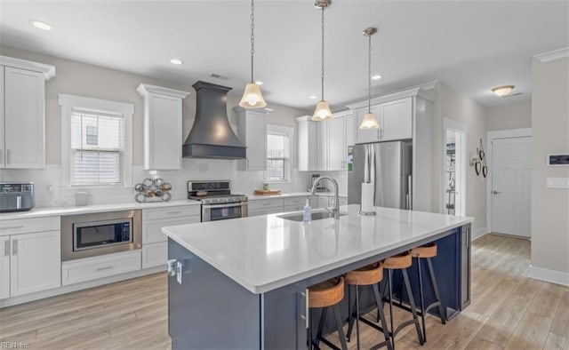 kitchen with premium range hood, stainless steel appliances, sink, pendant lighting, and white cabinetry