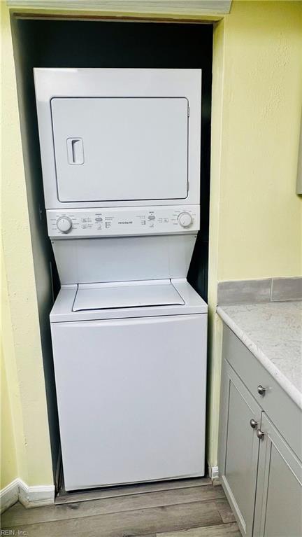 laundry area with light hardwood / wood-style flooring and stacked washing maching and dryer