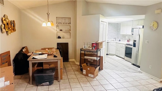 kitchen with stainless steel appliances, light tile patterned floors, white cabinets, hanging light fixtures, and lofted ceiling