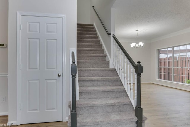 staircase with crown molding, wood-type flooring, a textured ceiling, and a notable chandelier