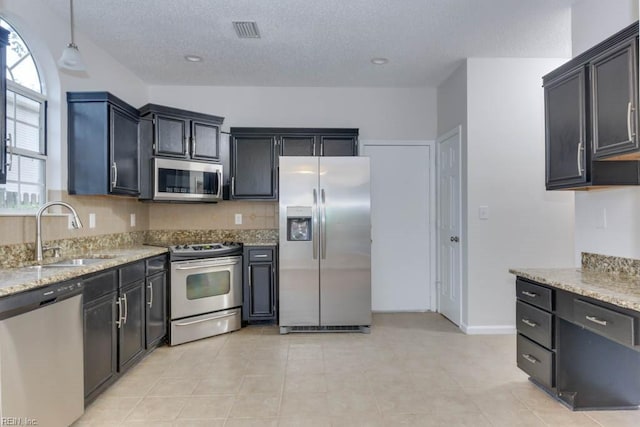 kitchen featuring pendant lighting, sink, light stone countertops, a textured ceiling, and stainless steel appliances