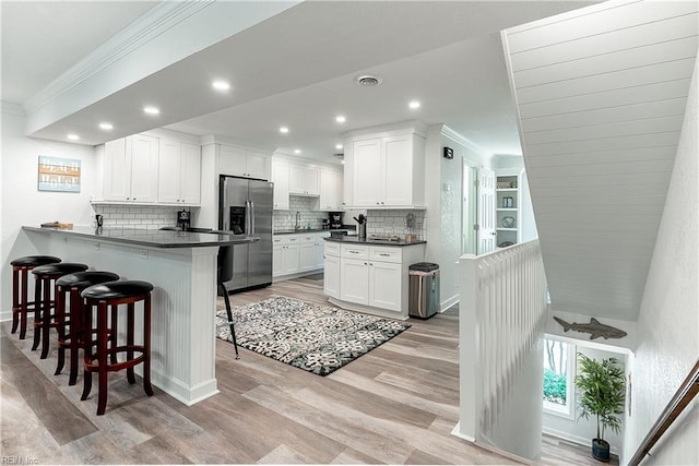 kitchen with stainless steel fridge with ice dispenser, kitchen peninsula, white cabinetry, and light hardwood / wood-style floors