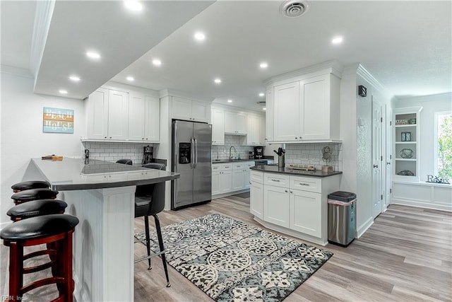 kitchen featuring a breakfast bar, white cabinets, light hardwood / wood-style flooring, stainless steel fridge, and ornamental molding