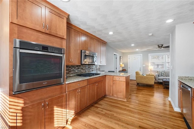 kitchen featuring kitchen peninsula, appliances with stainless steel finishes, light hardwood / wood-style floors, and light stone countertops