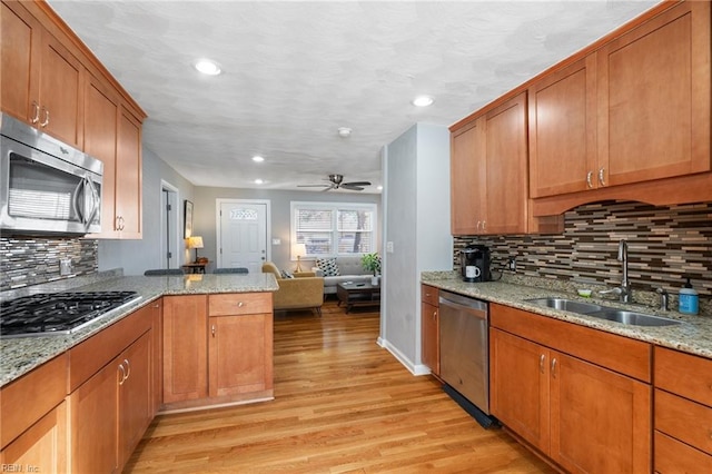 kitchen featuring light stone countertops, ceiling fan, sink, stainless steel appliances, and light hardwood / wood-style floors