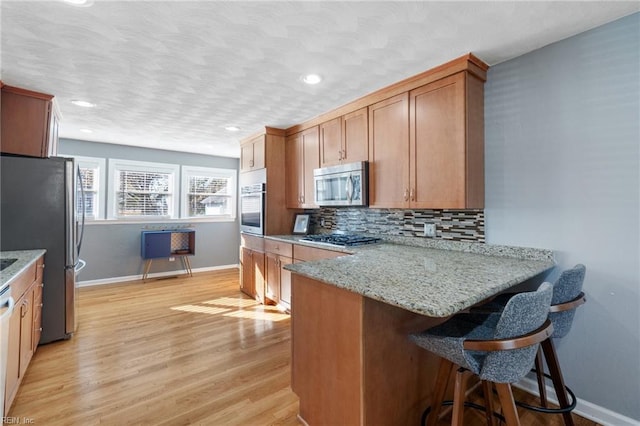 kitchen featuring a breakfast bar, light stone countertops, light wood-type flooring, kitchen peninsula, and stainless steel appliances