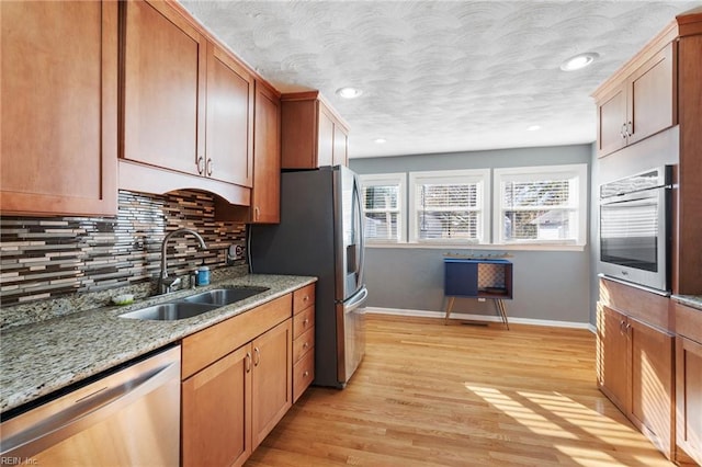 kitchen with appliances with stainless steel finishes, light wood-type flooring, tasteful backsplash, light stone counters, and sink