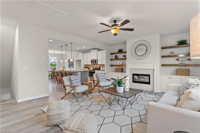 living room featuring a premium fireplace, ceiling fan, sink, and light hardwood / wood-style floors