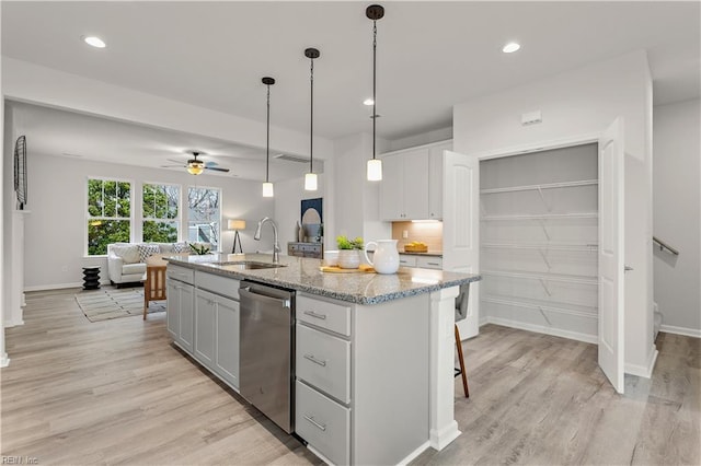 kitchen with light stone counters, a kitchen island with sink, ceiling fan, sink, and dishwasher