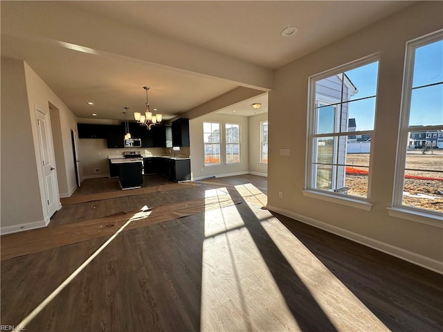 unfurnished living room with dark wood-type flooring, a healthy amount of sunlight, and a chandelier