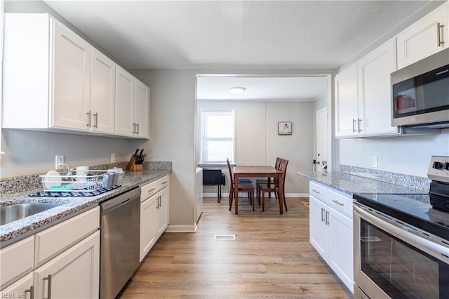 kitchen with light stone countertops, light wood-type flooring, white cabinetry, and stainless steel appliances