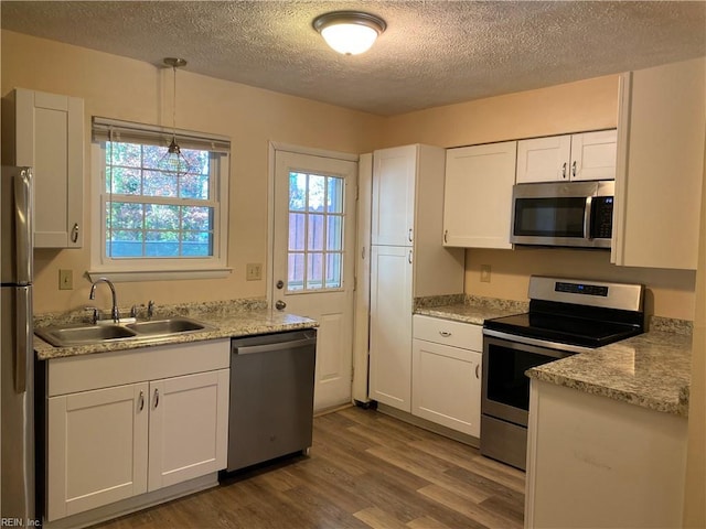 kitchen with white cabinetry, sink, stainless steel appliances, wood-type flooring, and decorative light fixtures