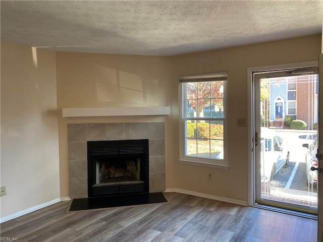 unfurnished living room featuring hardwood / wood-style floors, a textured ceiling, and a tiled fireplace