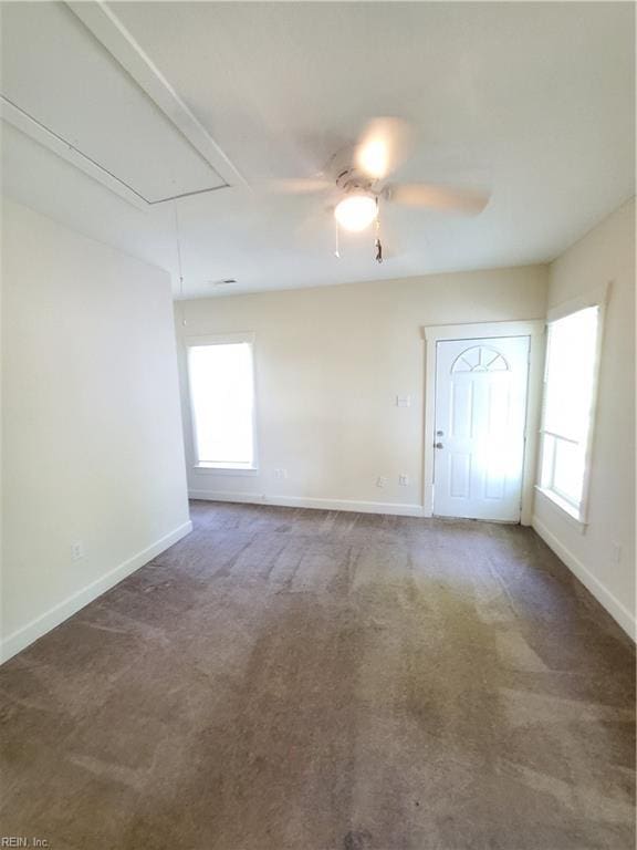 spare room with dark colored carpet, ceiling fan, and a wealth of natural light