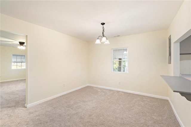 carpeted spare room featuring ceiling fan with notable chandelier and a healthy amount of sunlight