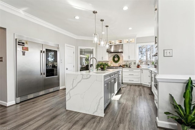 kitchen with stainless steel built in refrigerator, exhaust hood, sink, an island with sink, and white cabinetry