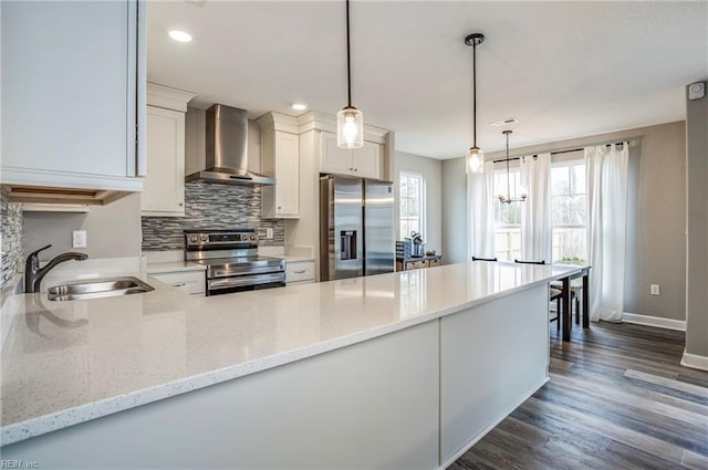 kitchen featuring appliances with stainless steel finishes, light stone counters, pendant lighting, and wall chimney range hood