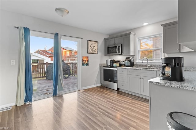 kitchen featuring gray cabinetry, sink, light stone counters, light hardwood / wood-style floors, and appliances with stainless steel finishes