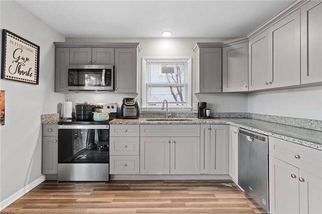 kitchen featuring gray cabinetry, sink, light wood-type flooring, appliances with stainless steel finishes, and light stone counters