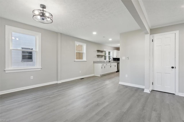 unfurnished living room featuring a notable chandelier, light hardwood / wood-style floors, sink, and a textured ceiling