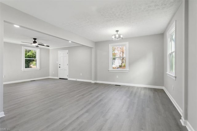 spare room with a textured ceiling, plenty of natural light, ceiling fan with notable chandelier, and hardwood / wood-style flooring