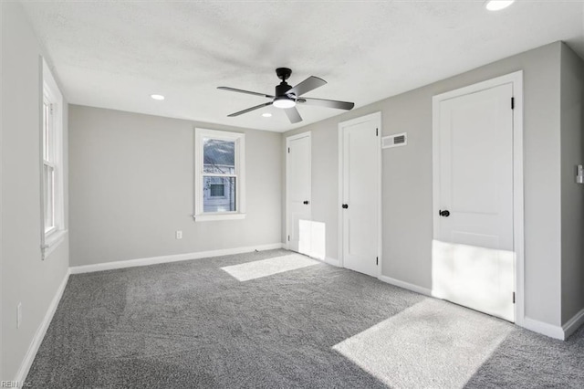 unfurnished bedroom featuring carpet, ceiling fan, and multiple closets