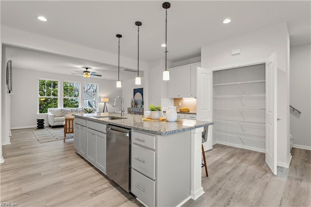 kitchen with dishwasher, a center island with sink, sink, ceiling fan, and light stone counters