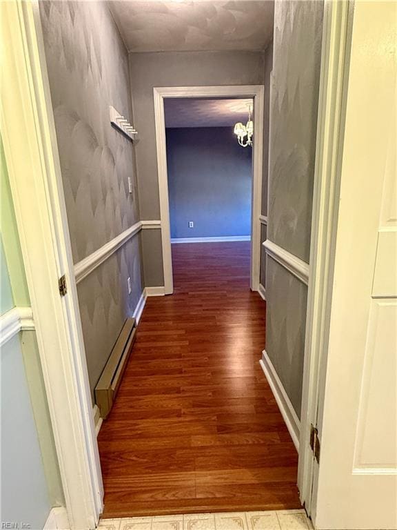 hallway with hardwood / wood-style floors, a baseboard radiator, and an inviting chandelier