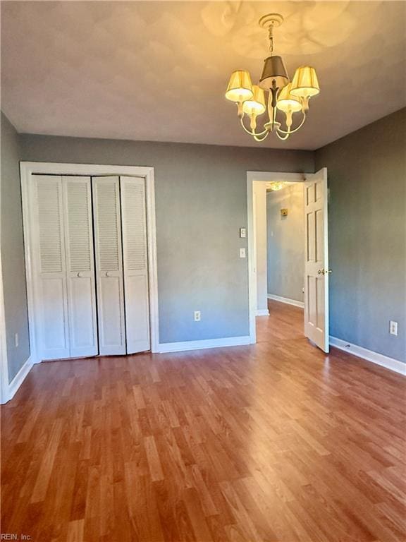 unfurnished bedroom featuring hardwood / wood-style flooring, an inviting chandelier, and a closet