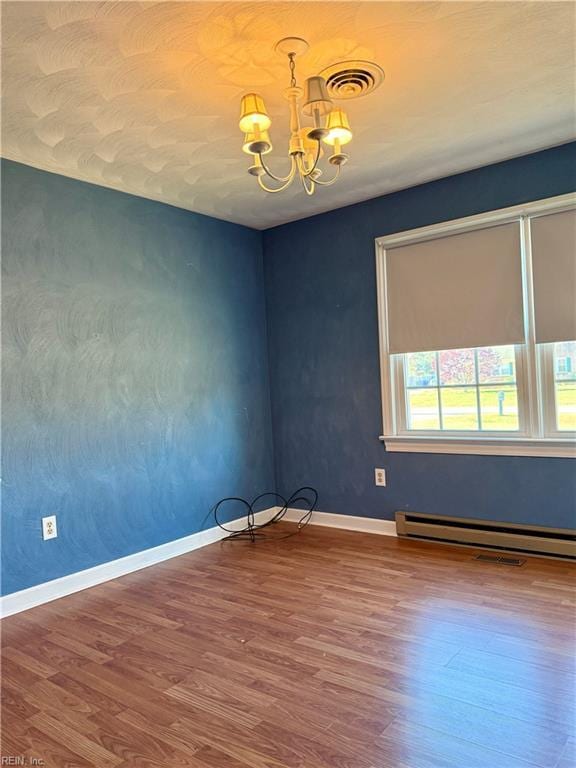 spare room with an inviting chandelier, a baseboard radiator, and hardwood / wood-style flooring