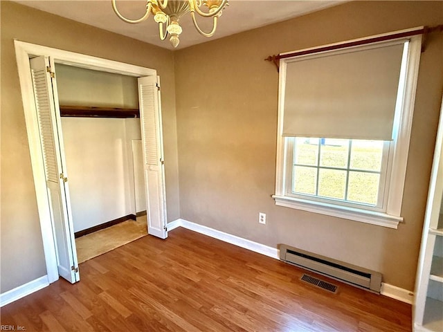 unfurnished bedroom with hardwood / wood-style floors, a closet, a baseboard heating unit, and a notable chandelier