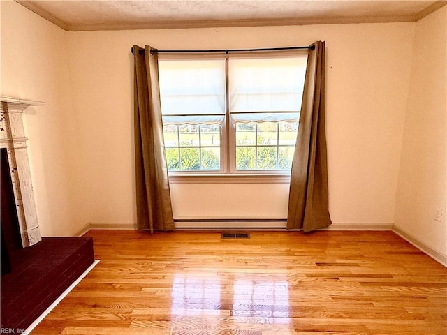 unfurnished living room featuring light hardwood / wood-style floors, a baseboard radiator, and crown molding