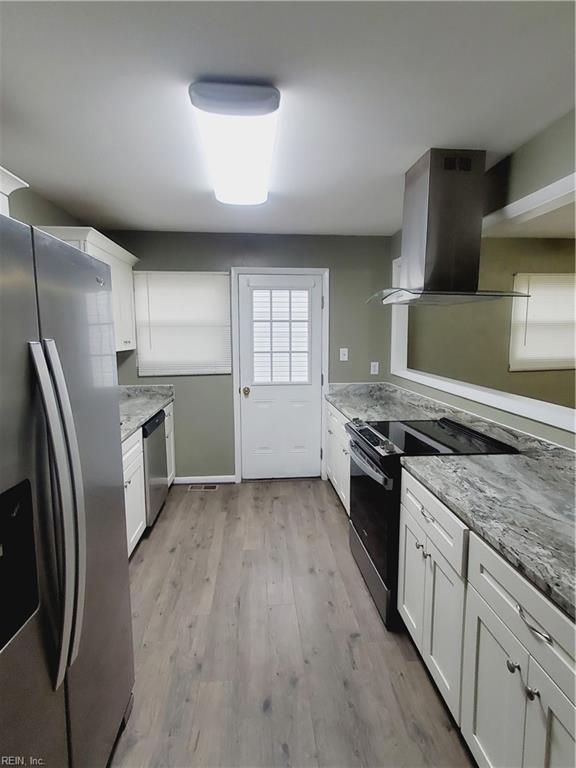 kitchen featuring white cabinets, light stone countertops, wall chimney range hood, and stainless steel appliances