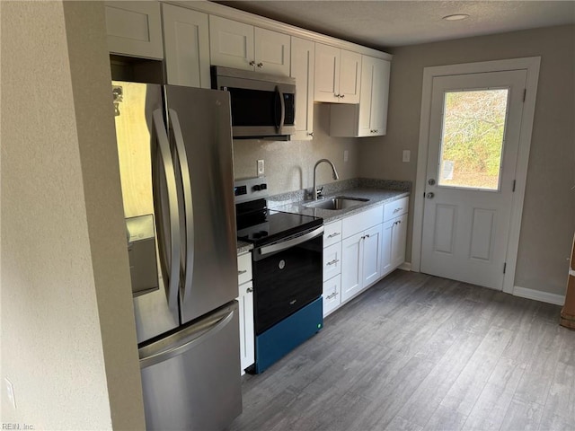 kitchen with stainless steel appliances, sink, white cabinets, and light hardwood / wood-style flooring