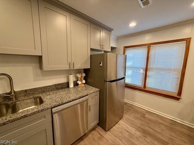 kitchen with appliances with stainless steel finishes, dark stone counters, sink, light hardwood / wood-style flooring, and gray cabinets